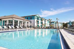 Flagler Beach apartment for rent - Luxury Apartments in Flagler Beach, FL, with In-Unit Washer and Dryer - Preserve at Flagler Beach - Resort Style Pool With Lounge Chairs, Palm Trees, Clubhouse, And Apartment Buildings.