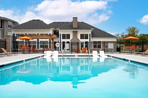 Wyoming apartment for rent - 2-Bedroom Apartments in Wyoming, MI - The Retreat - Outdoor Heated Swimming Pool with In-Water Loungers, Surrounded by Orange Loungers, Poolside Seating with Umbrellas, and Fence, Overlooking the Clubhouse and Apartments.