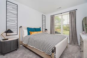 Wyoming apartment for rent - Wyoming, MI, Apartments with In-Unit Washer and Dryer - The Retreat Apartments - Bedroom With Upholstered Bed, Colorful Accent Pillows, Large Window, Gray Curtains, And Soft Carpet Flooring.
