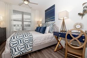 Atlanta apartment for rent - Pet-Friendly Luxury Apartments in Atlanta, GA - 1105 Town Brookhaven - Bedroom with Hardwood Floor, Bed, Desk with Chair and Lamp, Ceiling Fan, and Large Window.