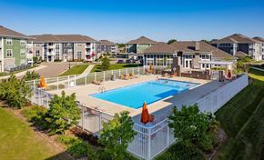 Kalamazoo apartment for rent - Kalamazoo, MI, Apartments for Rent - Parkway Flats - Aerial View of Heated Outdoor Saltwater Pool with Sun Deck, Surrounded by White Fence, Orange Loungers and Umbrellas, Overlooking the Landscaping, Clubhouse, and Apartments.