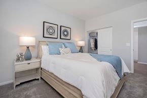 Middletown apartment for rent - Pet-Friendly Apartments in Middletown, OH - Echo Ridge Apartments - Modern Bedroom With Wood Bed Frame, White Bedding, Blue Accent Pillows, Bedside Lamps, Soft Carpet Flooring, And Open Closet.