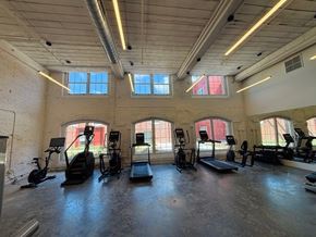 Warrenville apartment for rent - Two-Bedroom Luxury Apartments in Aiken, SC - Warren Mill Lofts - Fitness Club Equipped with Treadmills, Ellipticals, and a Stair Climber, Positioned on Concrete Floors with High Ceilings and Windows.