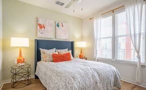 Tampa apartment for rent - Pet-Friendly Apartments in Tampa, FL - Havana Square - Bedroom with Vinyl Plank Flooring, Bed, Nightstands, Lamps, Wall Paintings, Ceiling Fan, and Large Windows with Coverings.