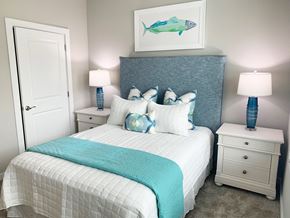 Pensacola apartment for rent - One-Bedroom Apartments in Pensacola, FL - Preserve at Perdido - Bedroom with a Textured Headboard-Bed Flanked by Two Nightstands with Lamps Set off with a Carpet, Oceanic Decor, and Neutral Walls.