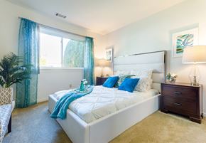Saginaw triplex for rent - Pet-Friendly Apartments in Saginaw, MI - Waters Landing Apartments - Spacious Bedroom With Upholstered Bed, Blue Accent Pillows, Nightstands With Lamps, and Large Window With Teal Curtains.