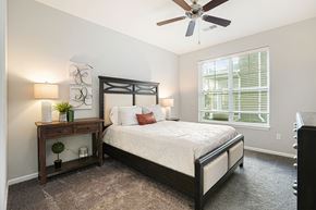 Grand Rapids apartment for rent - Three-Bedroom Apartments in Grand Rapids, MI - Knapp’s Corner Flats - Bedroom with Carpet Flooring, 9-Foot Ceiling, Ceiling Fan, Queen Size Bed, Nightstands, Lamps, Wall Arts, Decorative Plants, Dresser, and a Large Window with Blinds.
