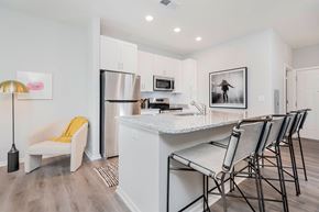 Jeffersonville apartment for rent - Luxury Apartments in Louisville, KY, with In-Unit Washer and Dryer - The Laurel Apartments - Kitchen With White Cabinetry, Stainless Steel Appliances, Granite Island Seating, And A Cozy Accent Chair.