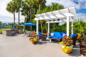 A white pergola is surrounded by blue couches and yellow vases