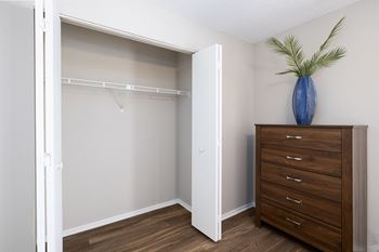 A room with a white closet and a brown dresser with a blue vase on top