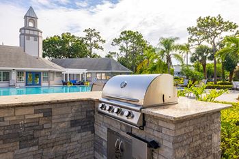 A barbecue grill is on a stone wall next to a swimming pool