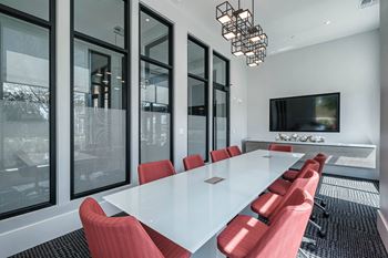 A conference room with a long white table and red chairs