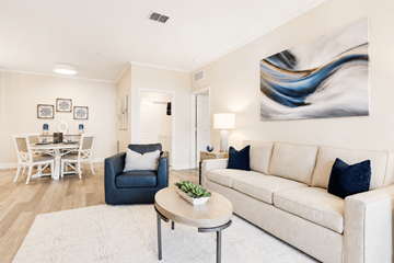 Jacksonville apartment for rent - A living room with a white couch, a blue chair, a dining table with chairs, a lamp, and a painting on the wall.