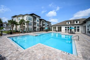 Pensacola apartment for rent - 1-Bedroom Apartments in Pensacola, FL - Preserve at Perdido - Resort-Style Swimming Pool Surrounded by Paver Deck, Furnished with Lounge Chairs, Tables with Umbrellas, and Apartment Building Backdrop.