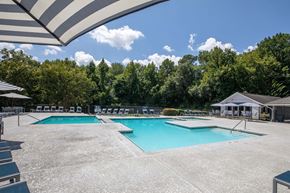 Norcross apartment for rent - A large outdoor swimming pool surrounded by trees and covered by a striped awning.