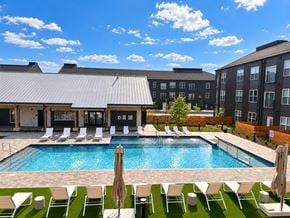 Rogers apartment for rent - A pool surrounded by chairs and umbrellas with a building in the background.