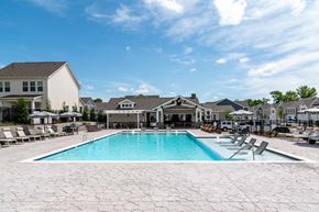 Gainesville apartment for rent - A swimming pool surrounded by a patio with chairs and a building in the background.