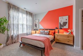Rockville apartment for rent - a bedroom with an orange accent wall and a bed with a wooden dresser and bedside