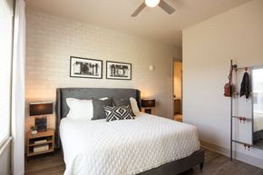 Memphis apartment for rent - 1 BR Apartments in Downtown Memphis TN - The Landing Residences - Furnsihed Bedroom wtih Hardwood Floor, Bed, Nightstands with Lamps, Standing Mirror with Storage, Ceiling Fan, White Painted Brick Accent Wall, and Attached Bathroom
