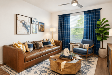 Fort Worth apartment for rent - A living room with a brown leather couch, a coffee table with a gift box on it, a blue chair, and a ceiling fan.