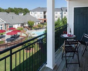 Sterling apartment for rent - A balcony with a table set for two overlooks a pool and apartment buildings.