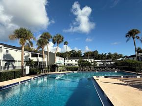 Daytona apartment for rent - A swimming pool surrounded by palm trees and buildings.