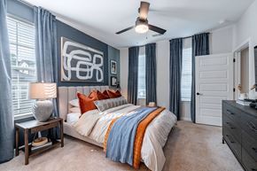Greenville apartment for rent - Greenville, SC, Luxury Apartments with an In-Unit Washer and Dryer - Evolve Homestead Apartment Homes - Bedroom with Large Bed, Carpet Flooring, Nightstand, Lamp, Ceiling Fan, and Dresser.