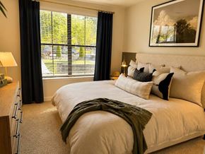 Atlanta apartment for rent - Luxury Apartments in Atlanta, GA, With In-Unit Washer and Dryer - The Eliza on Collier - Bedroom With Large Window, Plush Carpet, Lamps, Framed Wall Art, and Wood Dresser.