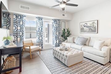 Fort Worth apartment for rent - A living room with a white couch, a wooden chair, a white ottoman, and a painting on the wall.