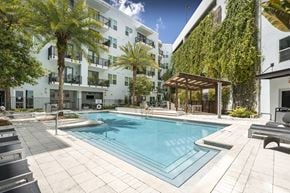 Tampa apartment for rent - A pool surrounded by palm trees and a white building with a green wall.
