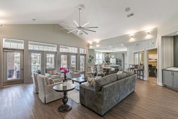 Easley apartment for rent - A spacious living room with a grey sofa, a round table with a flower on it, and a ceiling fan.