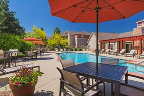 Colorado Springs apartment for rent - A poolside table with chairs and an umbrella overlooking a pool.
