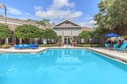 Tallahassee apartment for rent - A swimming pool in front of a building with a blue umbrella and chairs.