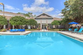 Tallahassee apartment for rent - A swimming pool in front of a building with a blue umbrella and chairs.