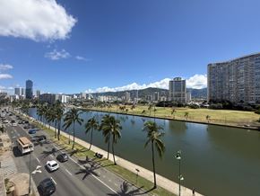 Honolulu condo for rent - A city street with cars and palm trees alongside a river.