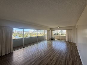 Honolulu condo for rent - A room with wooden floors and a view of the city through large windows.