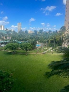 Honolulu condo for rent - a large grassy area with palm trees and a pool in the background