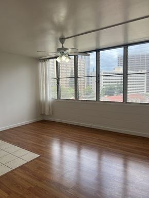 Honolulu apartment for rent - A room with a ceiling fan and a large window overlooking a cityscape.
