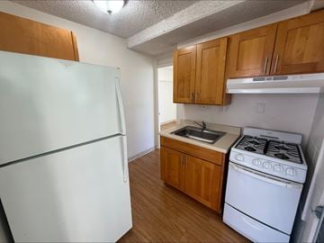 Honolulu apartment for rent - A white refrigerator sits next to a white stove in a kitchen with wooden cabinets.