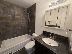 Honolulu condo for rent - A bathroom with a tiled shower, a white toilet, a sink and a bathtub.
