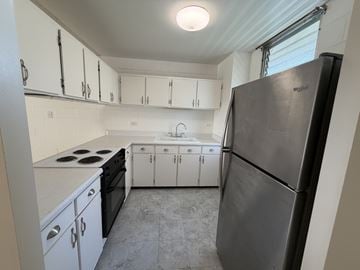 Honolulu condo for rent - A kitchen with white cabinets and a black refrigerator.