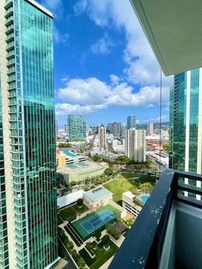 Honolulu condo for rent - A view from a high-rise building looking down at a cityscape with a pool area in the foreground.