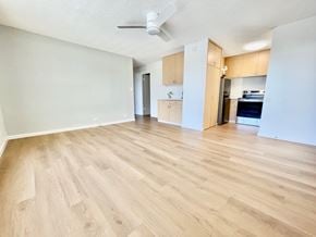 Honolulu condo for rent - A room with wooden flooring and a kitchen area in the background.