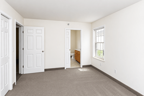 South Burlington apartment for rent - A room with a carpeted floor, a white door, a window with a white frame, and a wooden cabinet.