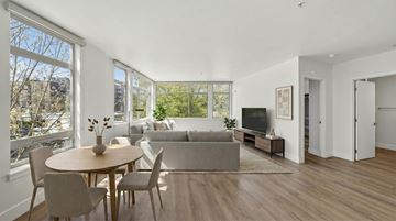 Seattle apartment for rent - A living room with a grey couch, a wooden table and chairs, and a television.