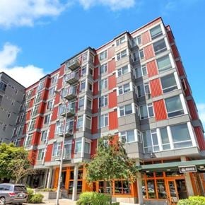 Seattle apartment for rent - A modern multi-story building with red and grey exterior and a green awning.