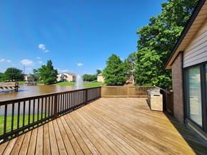 Stillwater apartment for rent - A wooden deck overlooks a body of water with a house and trees in the background.