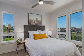 Portland apartment for rent - A bedroom with a large bed, a ceiling fan, and a view of a city skyline through the windows.