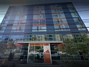 Seattle apartment for rent - A tall building with a glass facade and a red and white entrance sign.