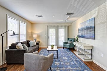 Suffield apartment for rent - A living room with a grey couch, a grey armchair, a coffee table, a blue rug, and a painting on the wall.